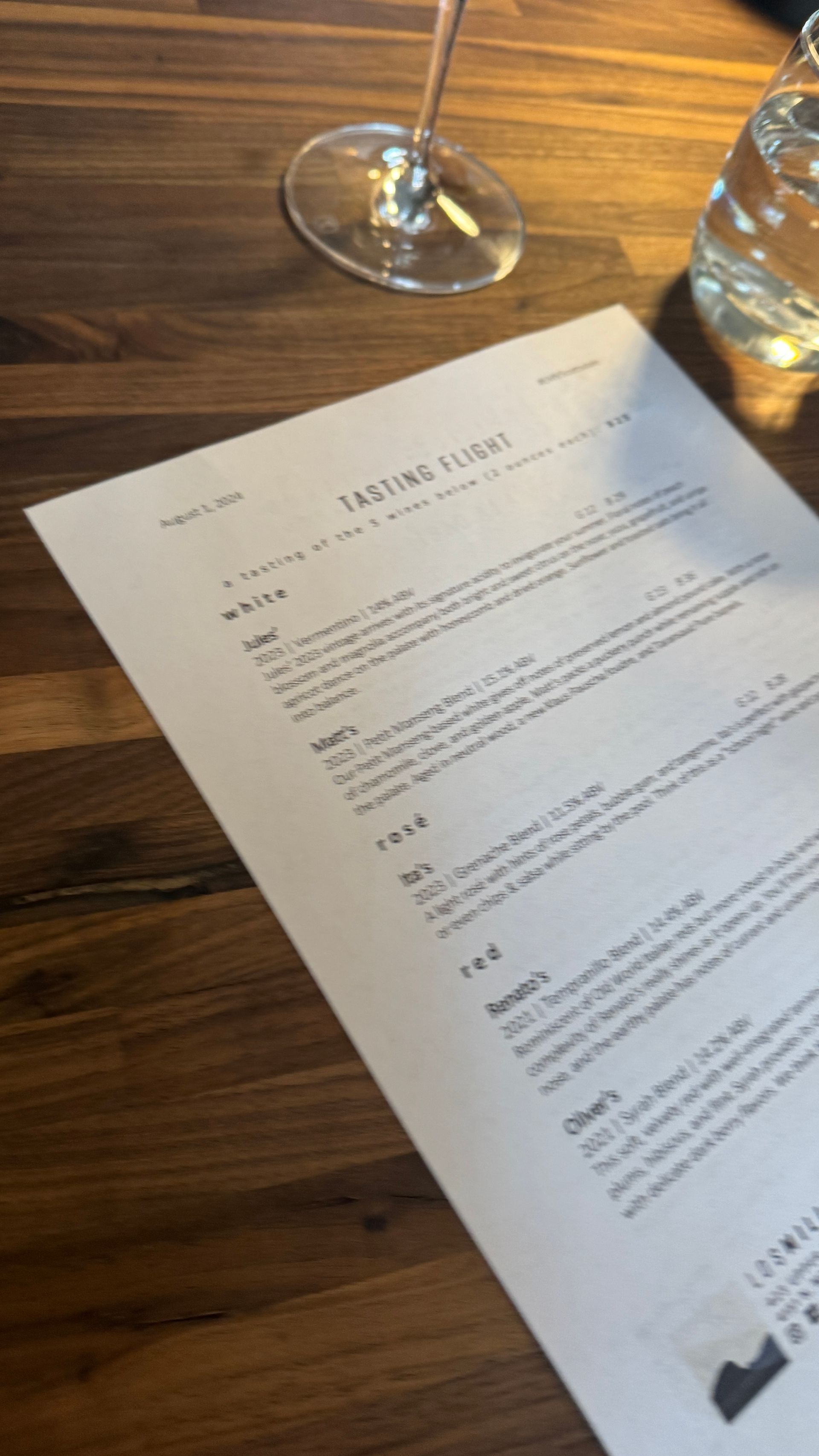 A menu is sitting on a wooden table next to a glass of wine.