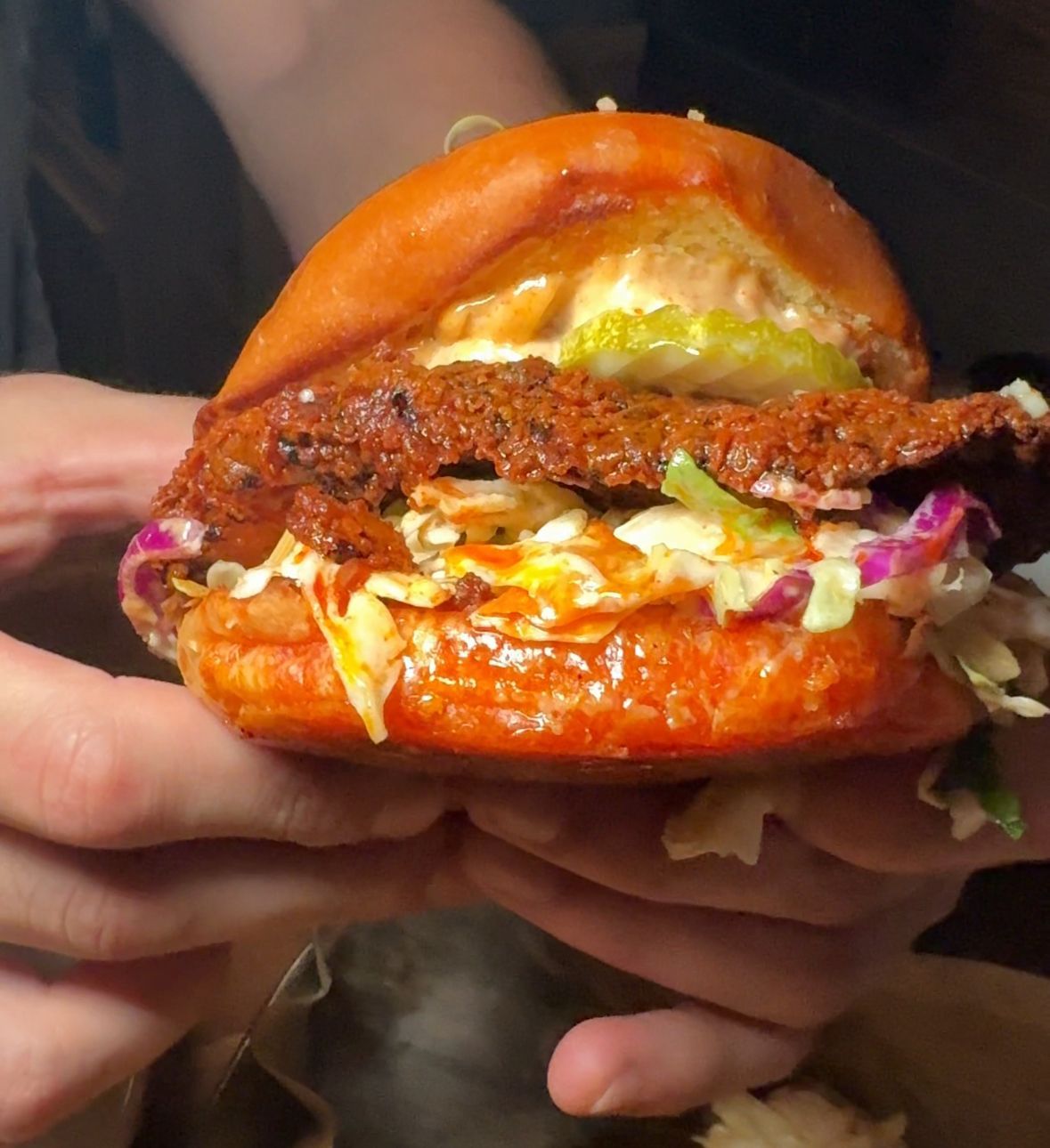 A person is holding a fried chicken sandwich with coleslaw
