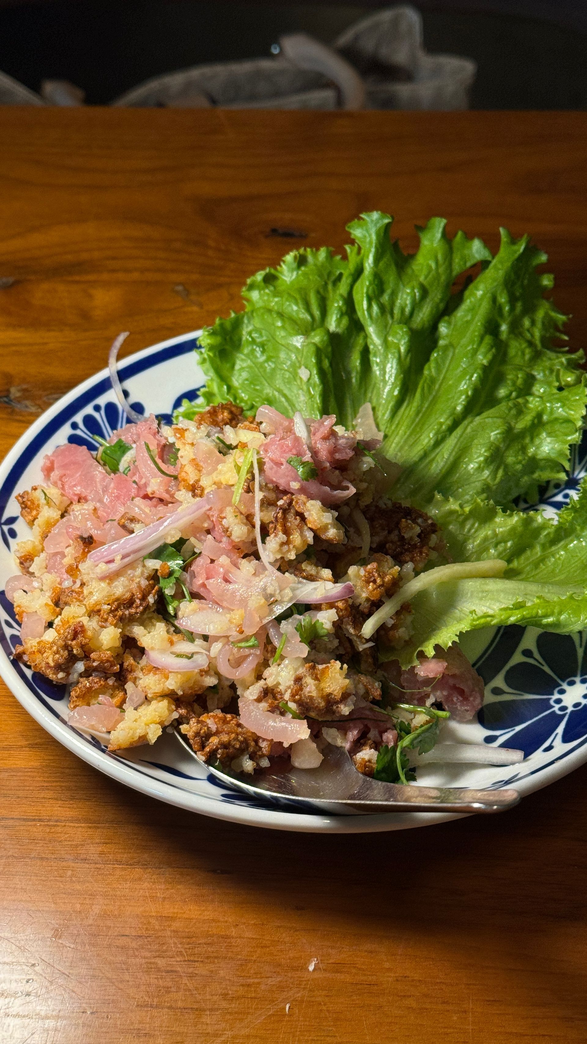 A plate of food with lettuce and meat on a wooden table.