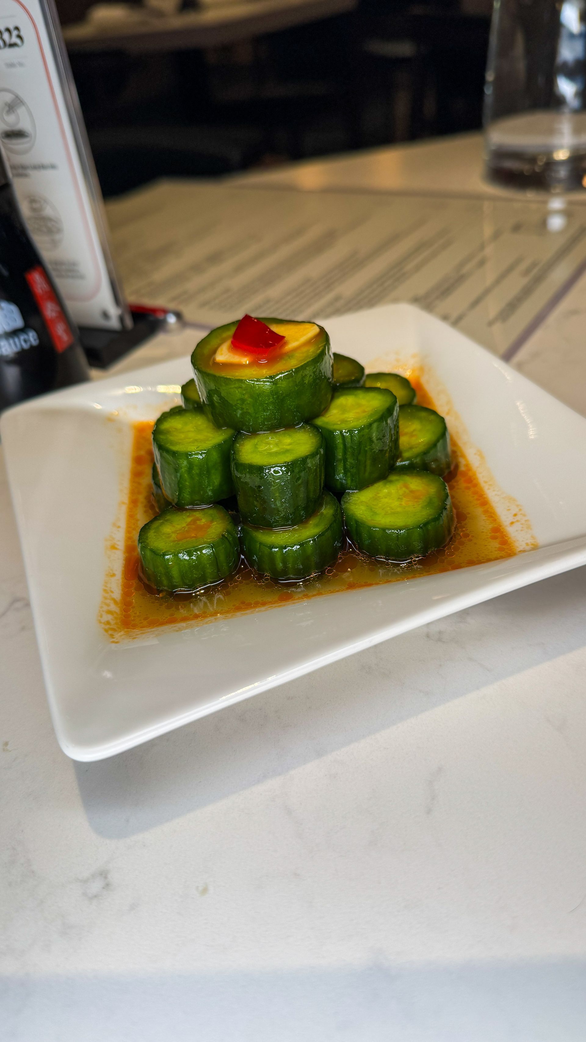 Stacked cucumber appetizer with red garnish on a white square plate