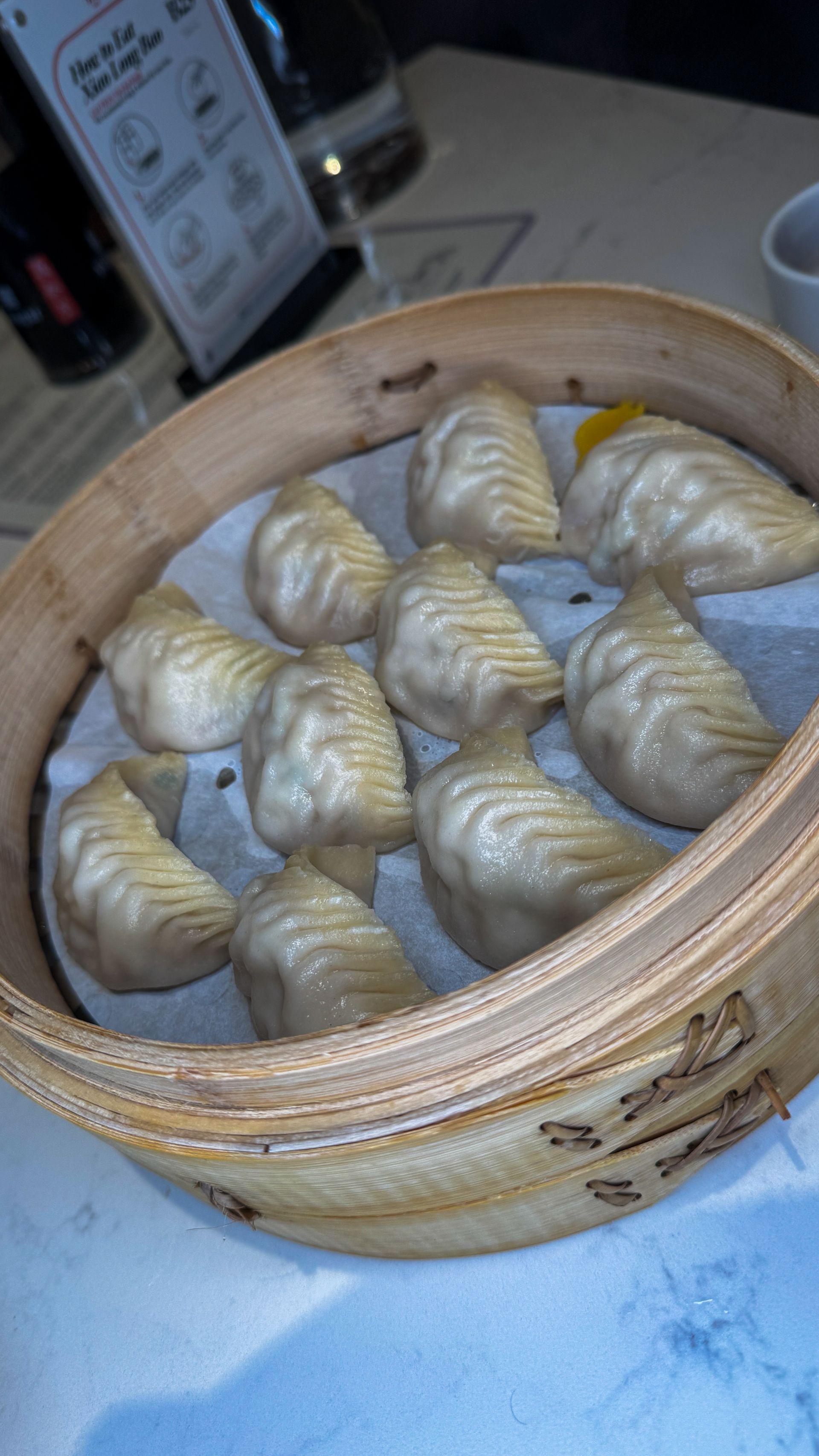 Steamed dumplings in a bamboo basket on a table, with a cup nearby.