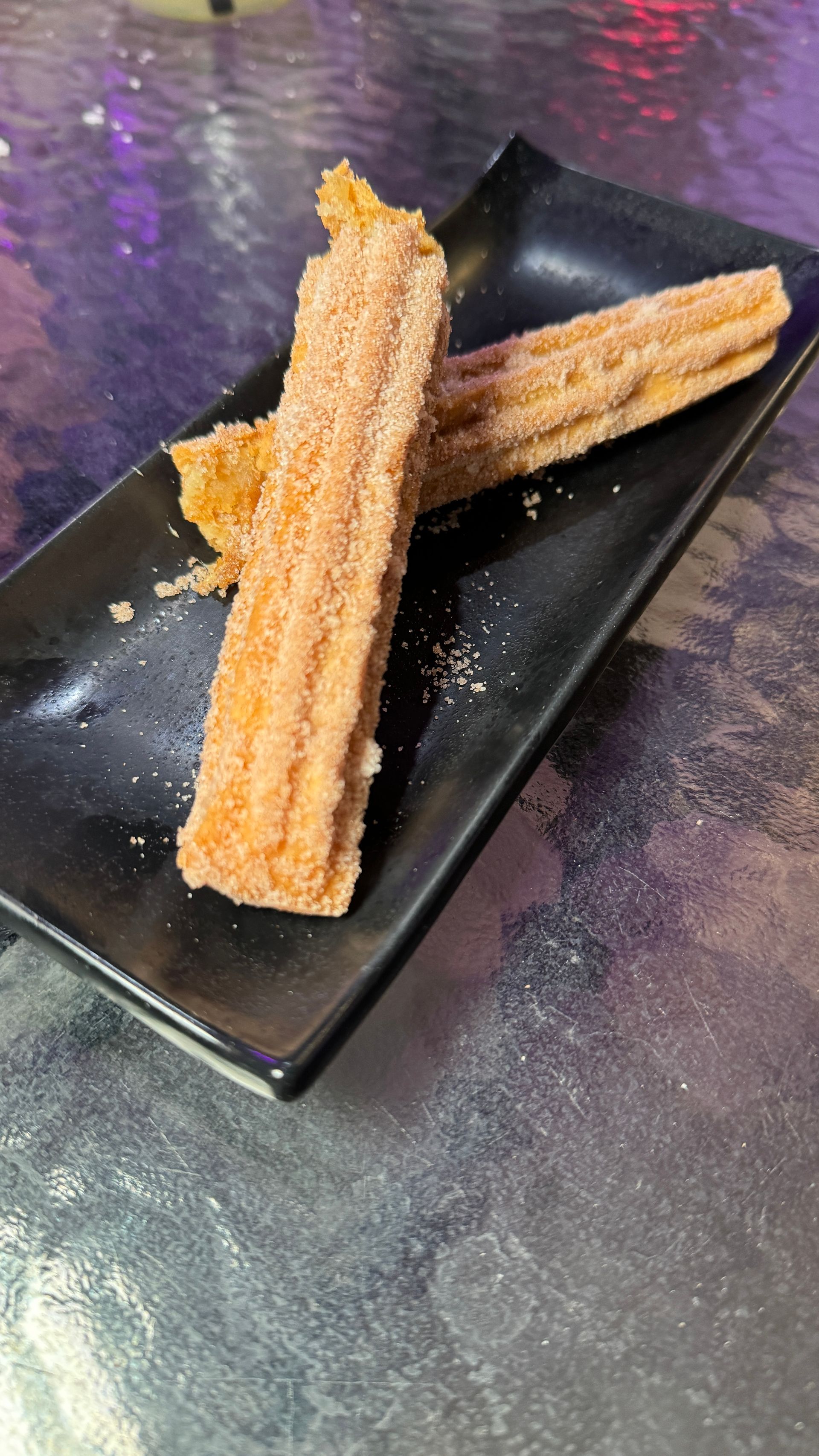 Two churros are on a black plate on a table.