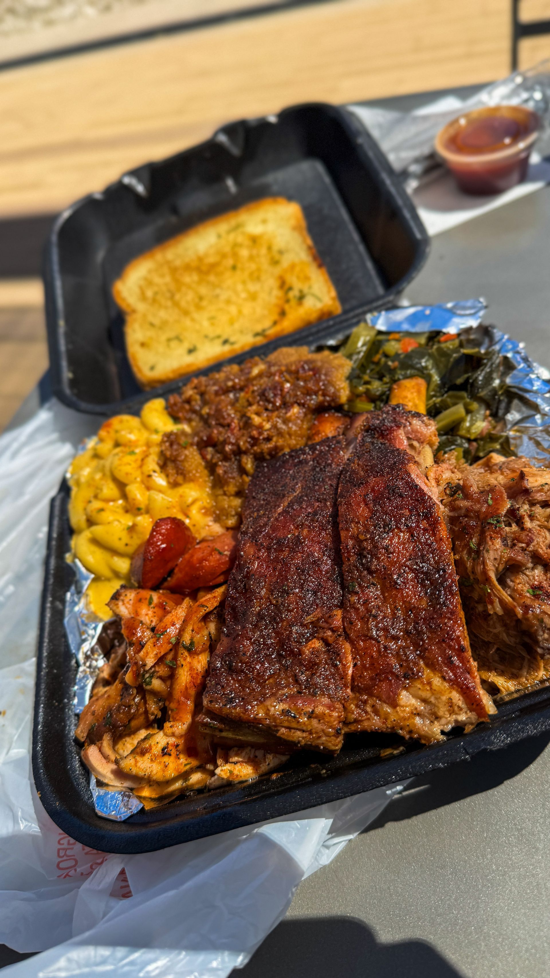 Takeout tray with grilled fish, mac and cheese, collard greens, beans, and cornbread on a table