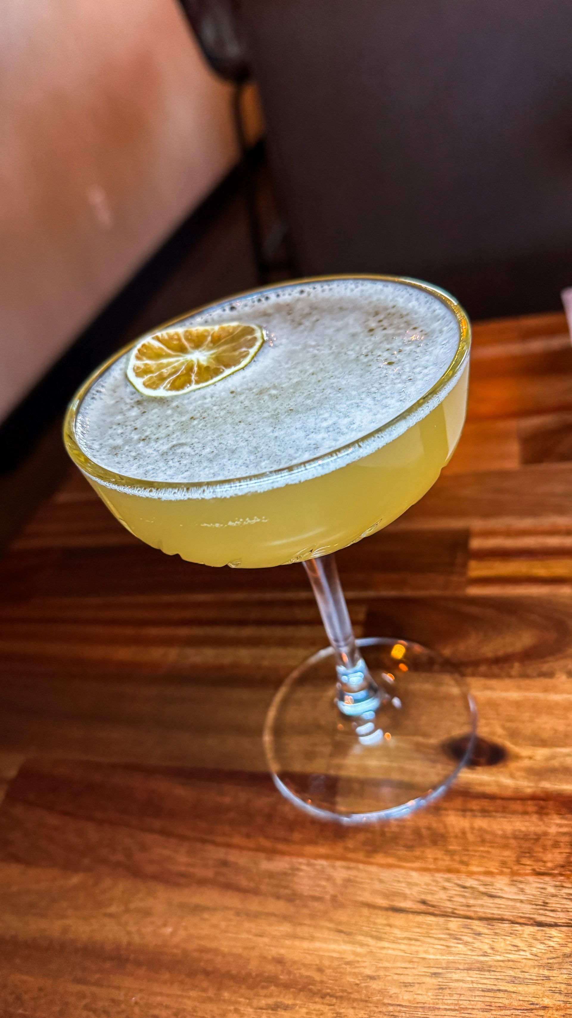 Yellow cocktail with a dried citrus garnish in a coupe glass on a wooden table.