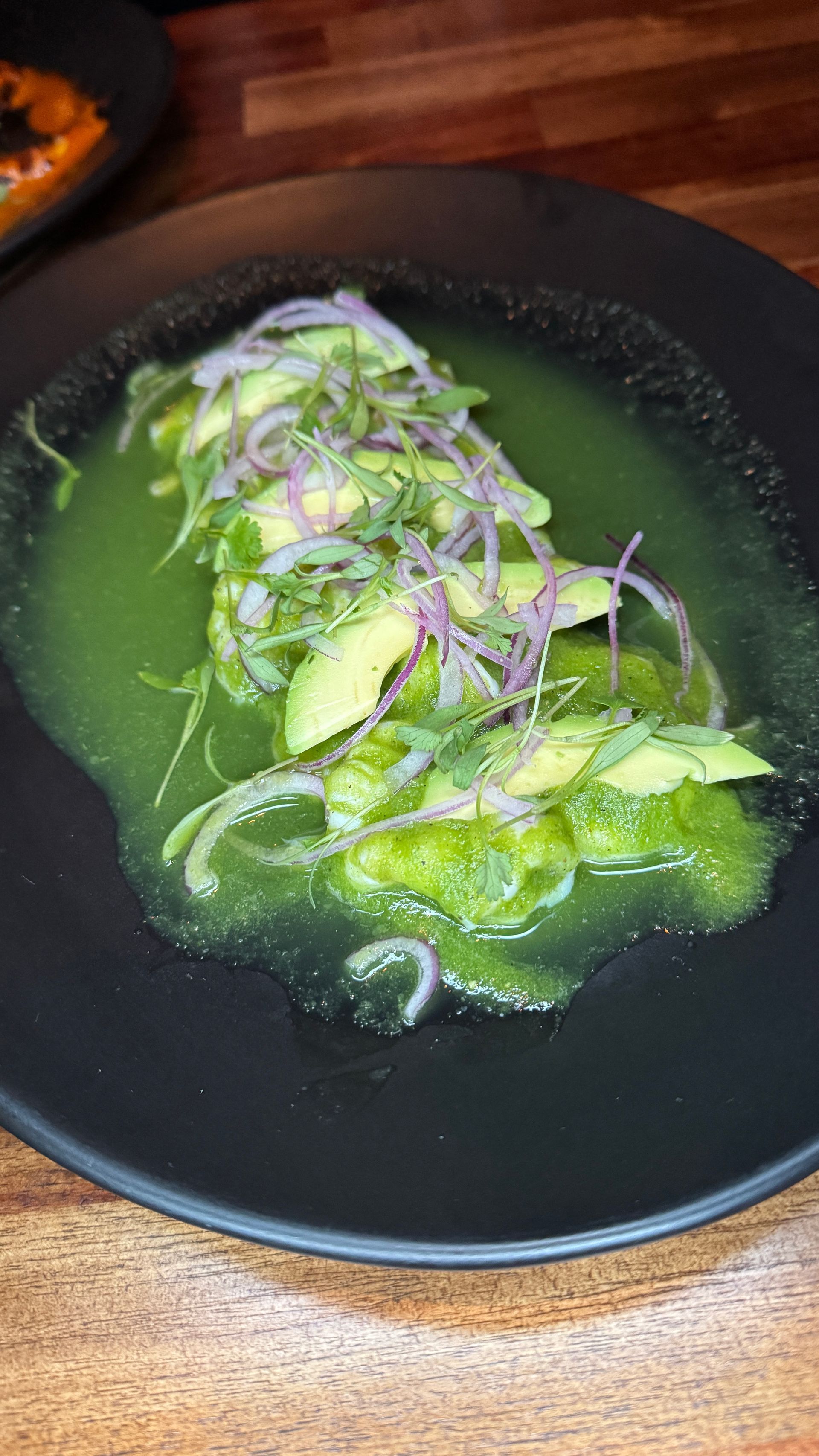 Green salad with purple onions on a black plate, served in a shallow broth on a wooden table