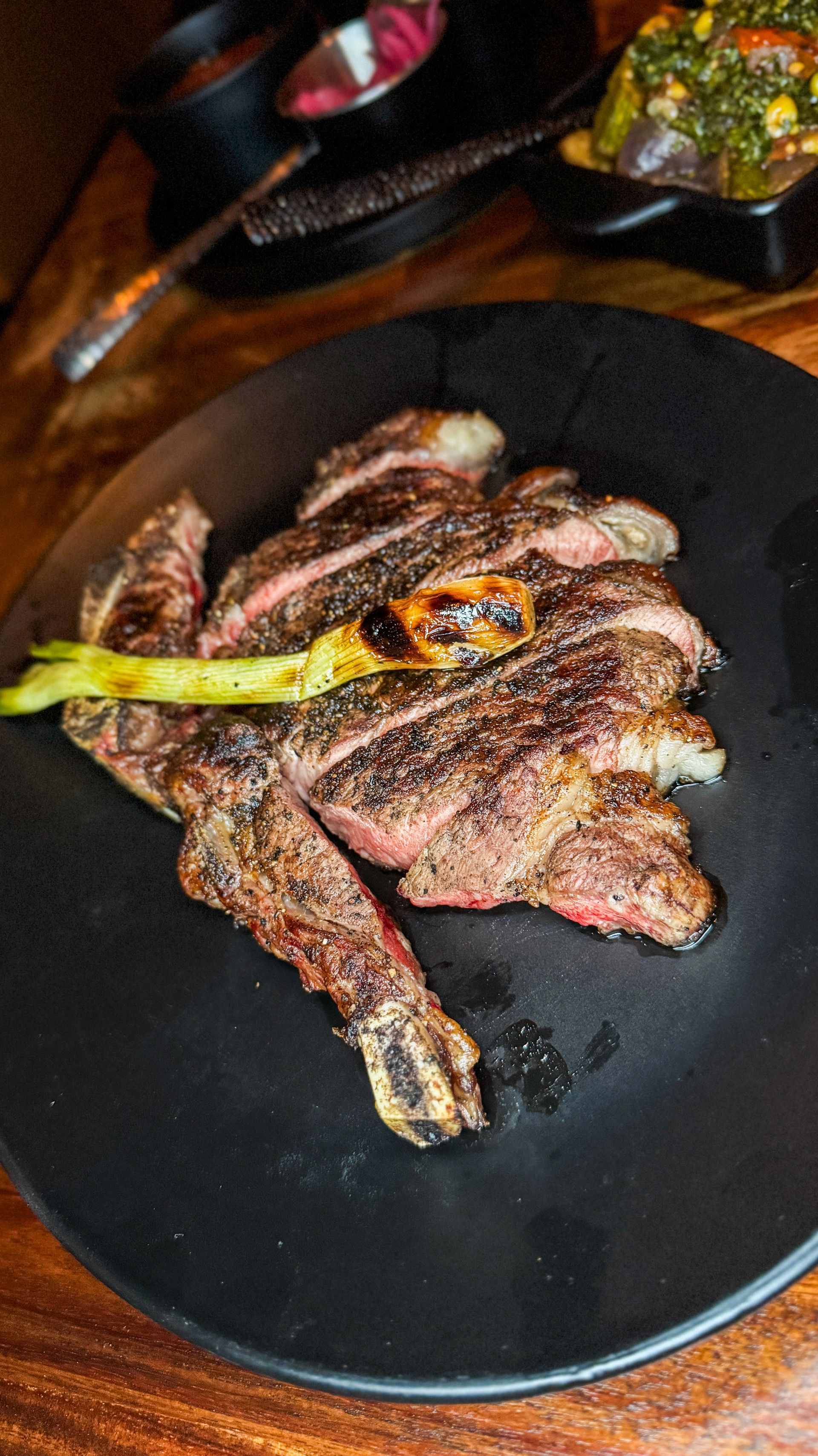 Grilled meat served on a black plate with green garnish on a wooden table