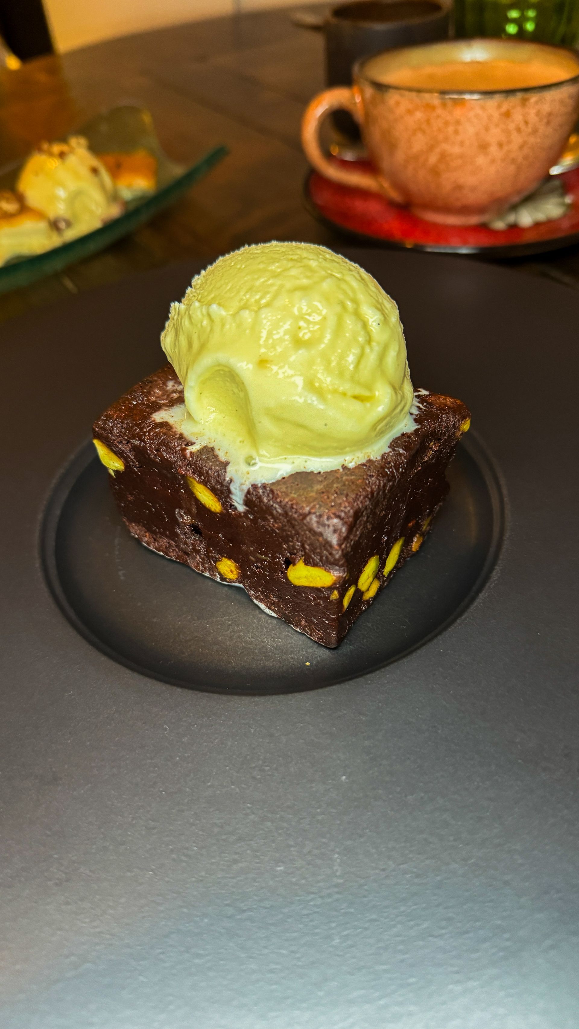 Chocolate brownie dessert topped with green ice cream on a black plate