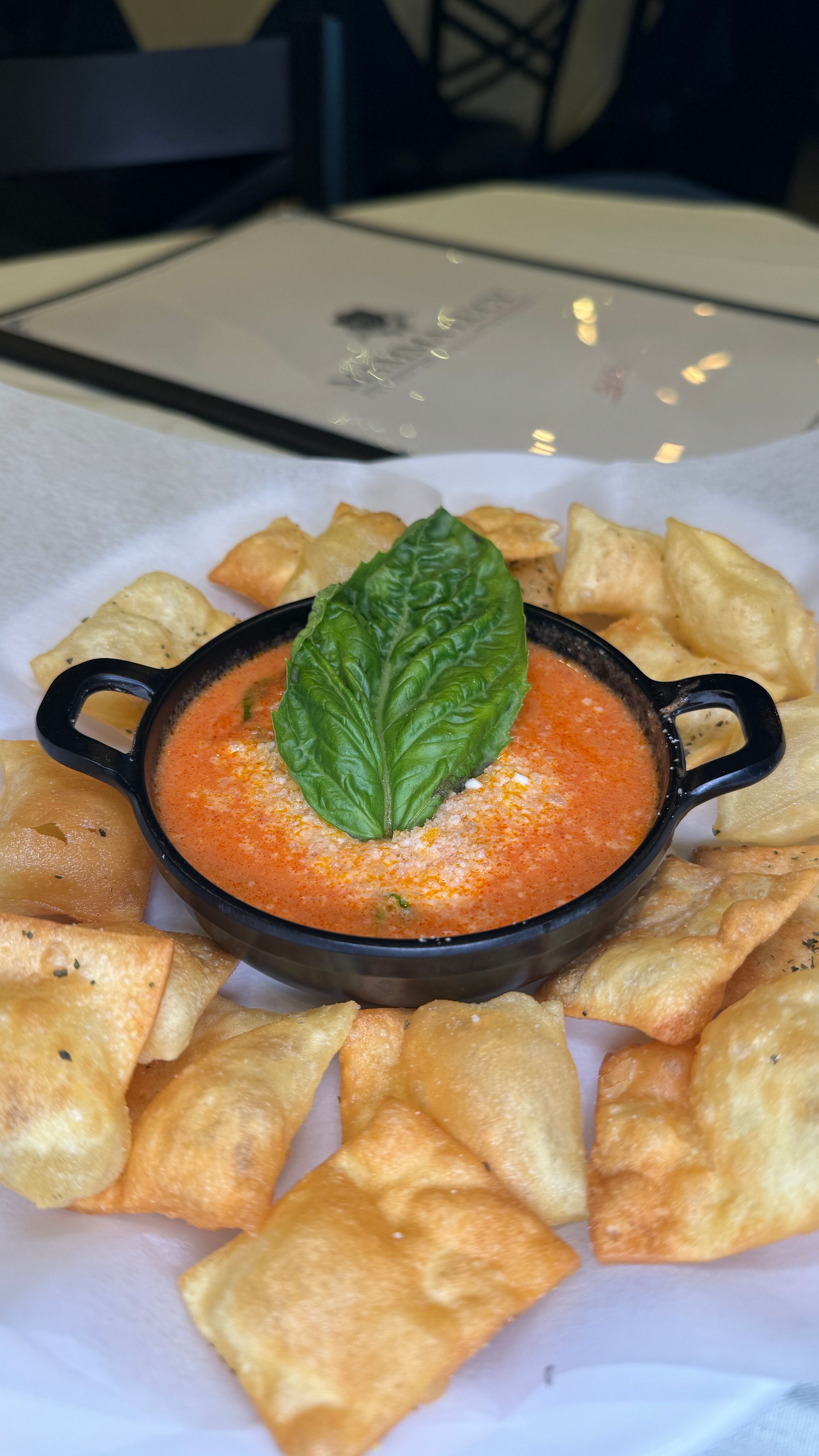 Bowl of red dip topped with basil leaf, surrounded by fried, golden pita chips.