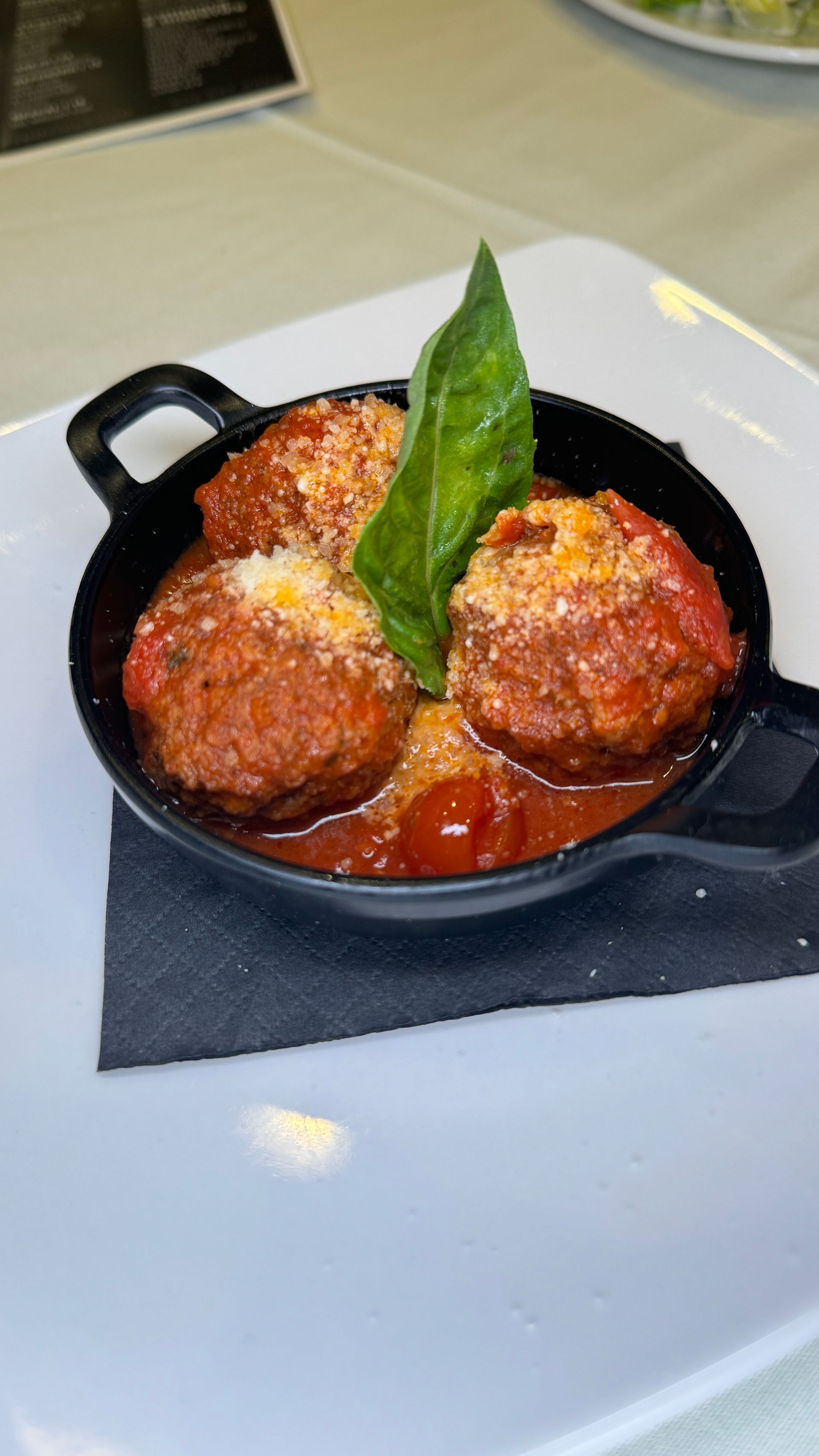 Meatballs in marinara sauce, topped with cheese and basil, served in a small black skillet on a white plate.