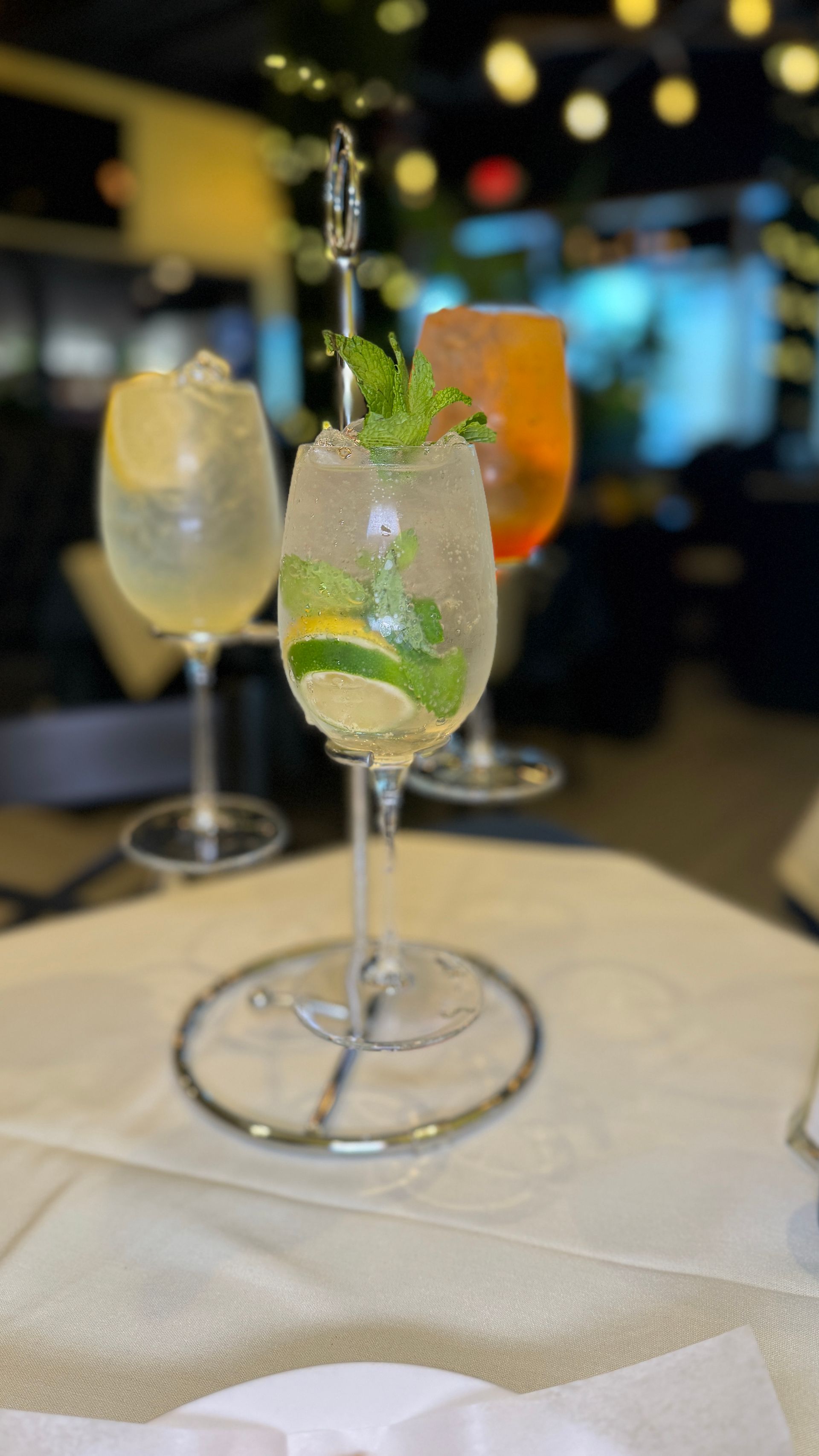 Three cocktails in stemmed glasses on a tiered server; mint garnish, citrus fruit, bubbly drinks.