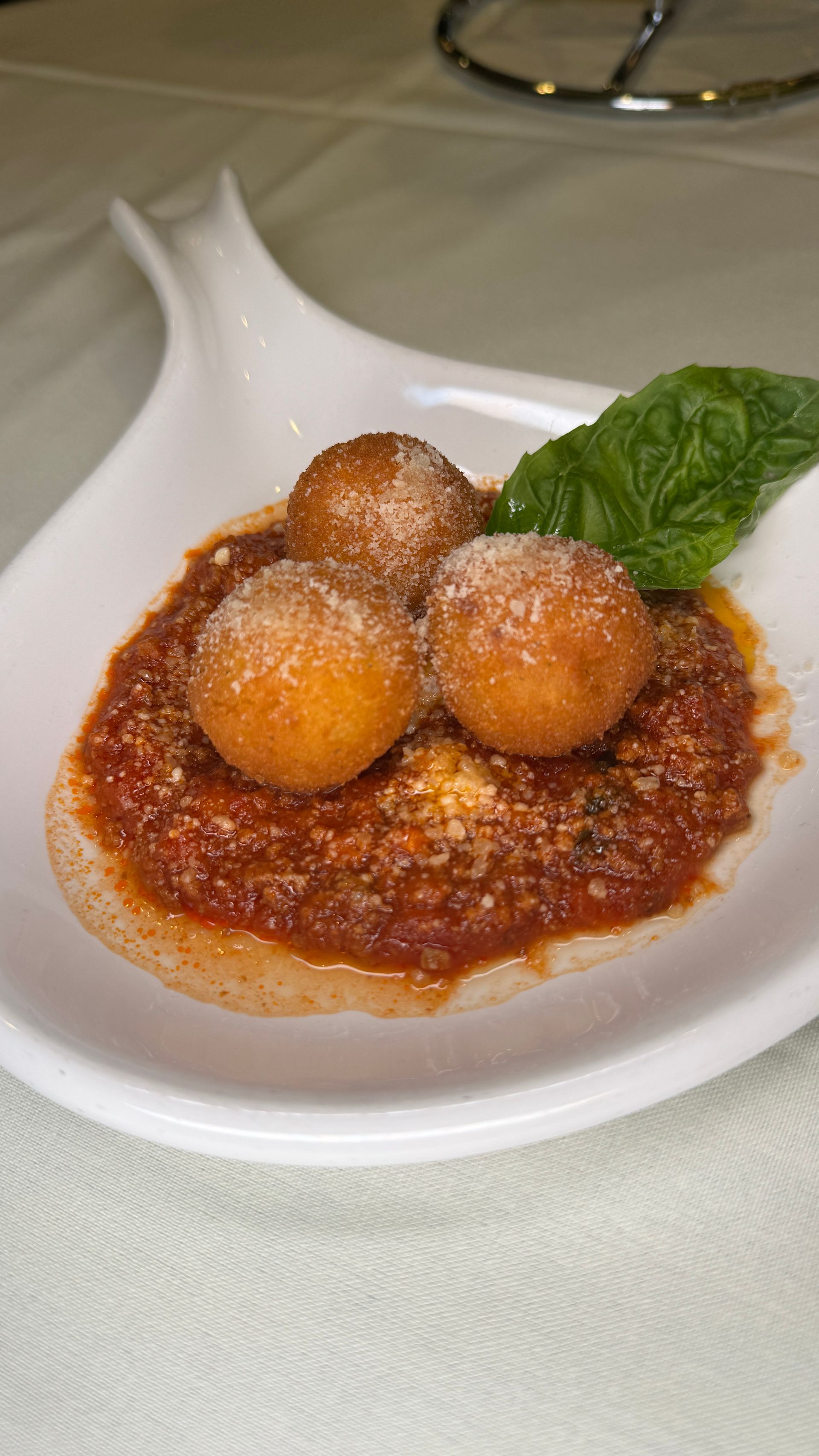 Three golden fried balls atop tomato sauce, sprinkled with cheese and basil, served on a white dish.