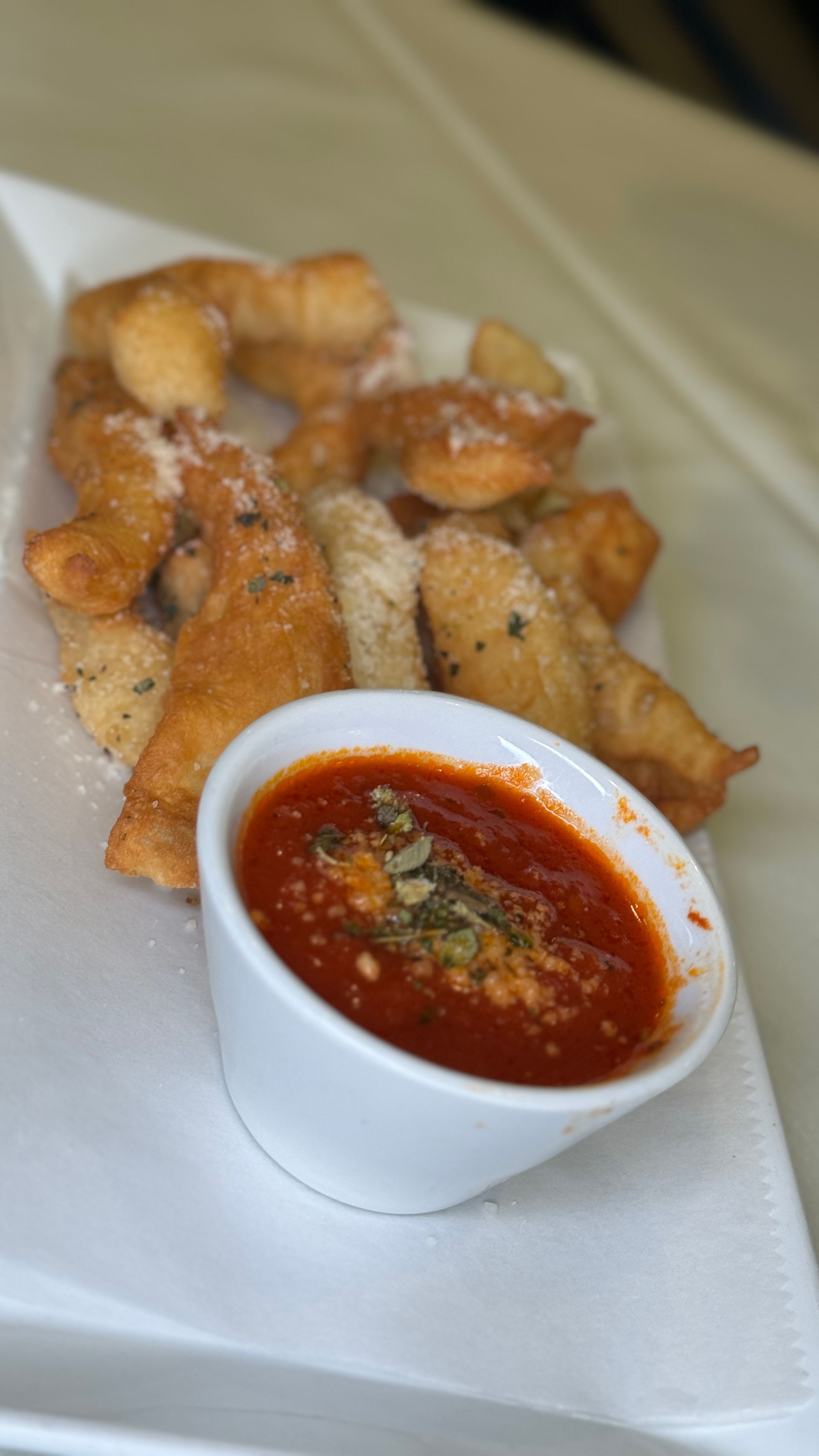 Fried dough with marinara sauce in a white bowl, served on a white plate.