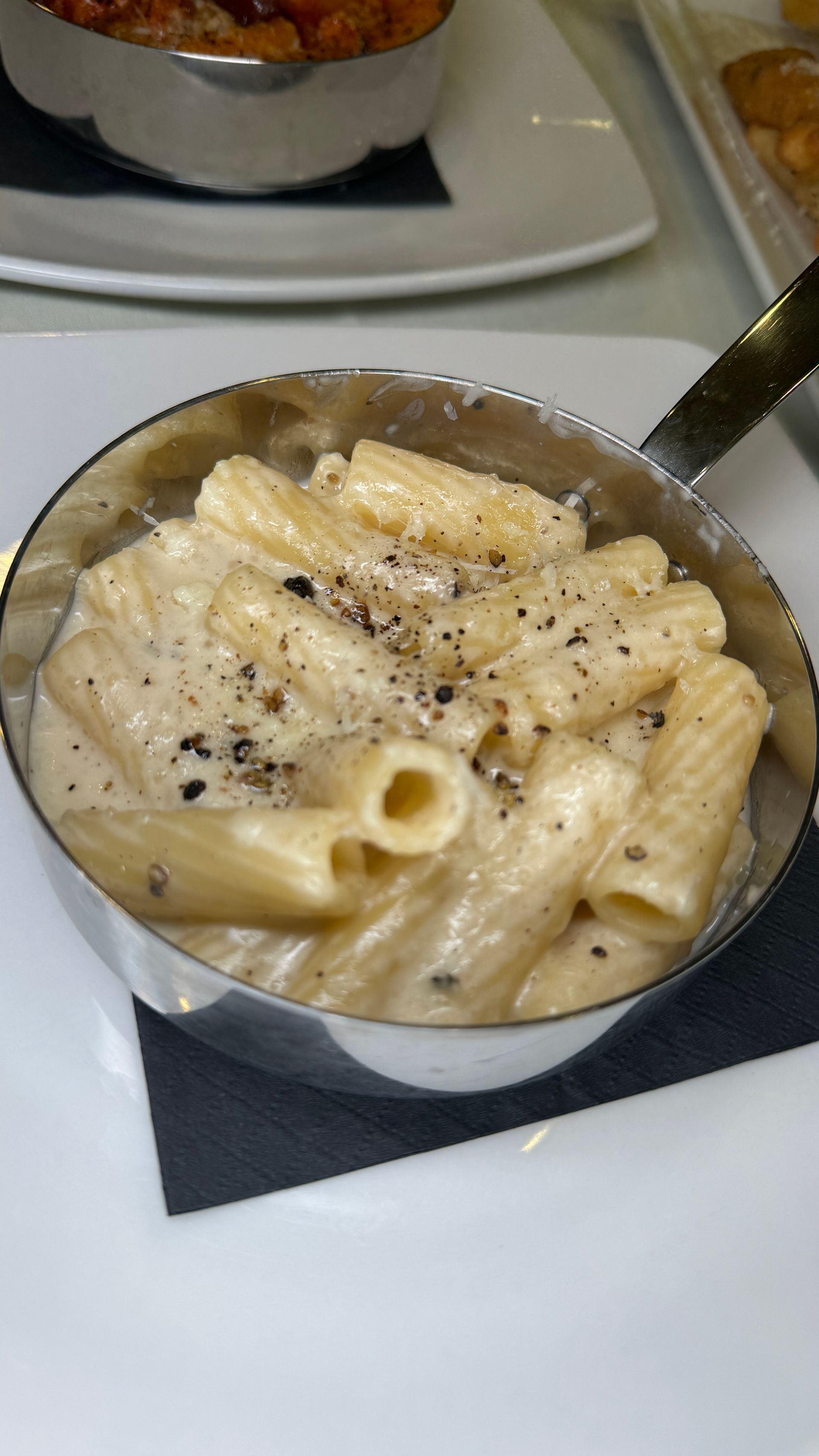 Pasta dish in small metal pan, creamy sauce, sprinkled pepper, on white plate.