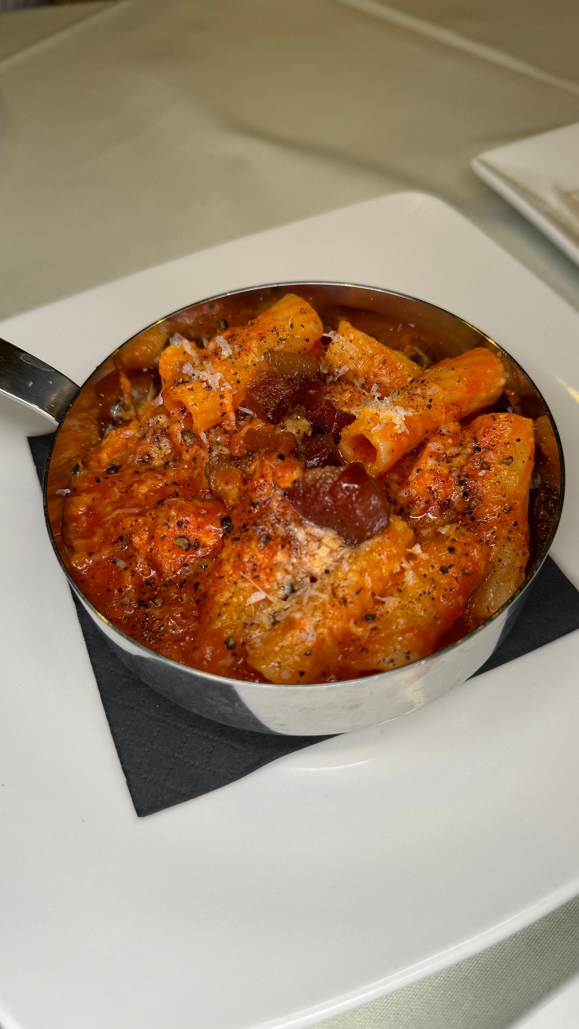 Pasta dish in a small, metal pot on a white plate.