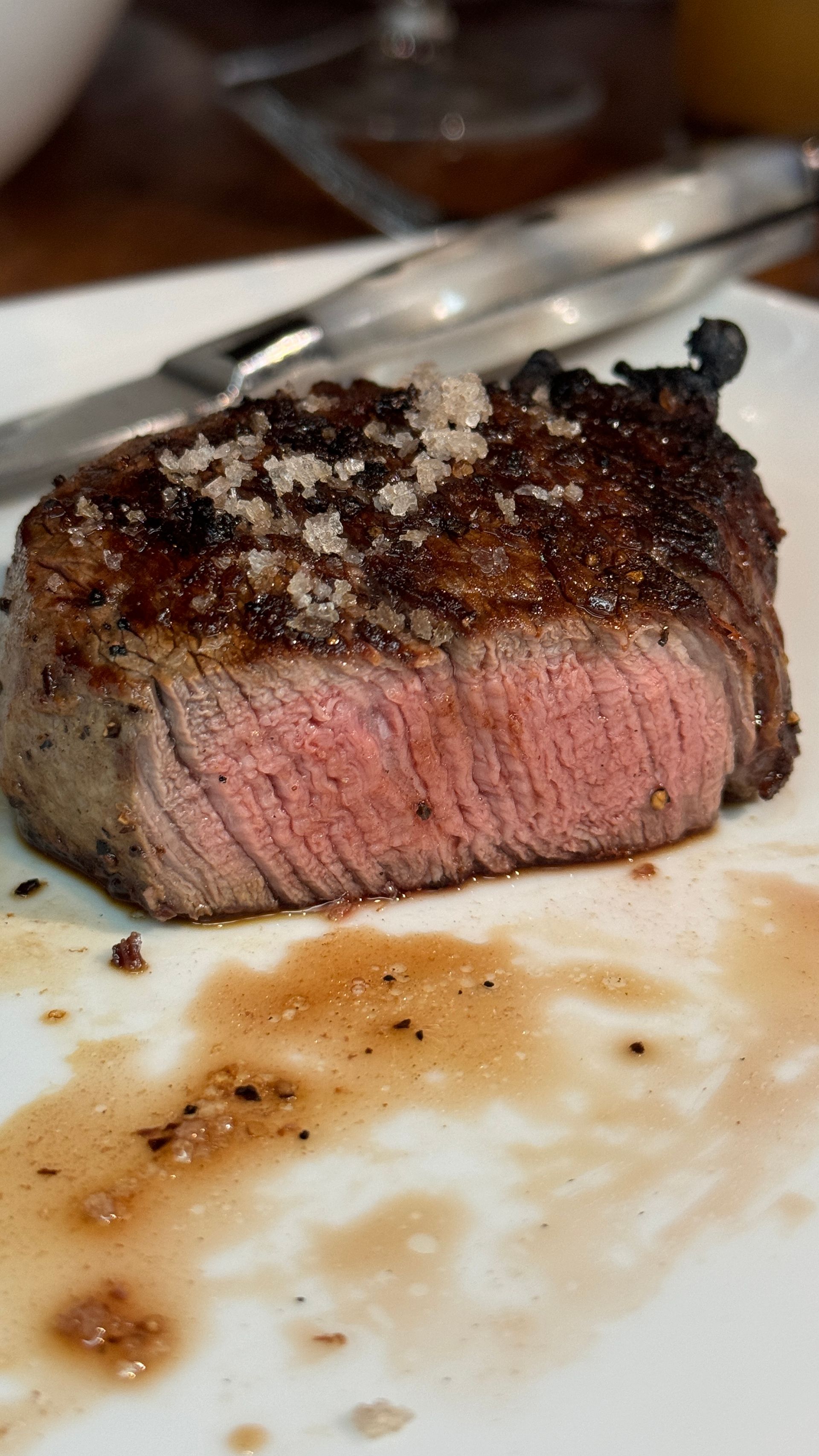 Sliced, medium-rare steak on a white plate, seasoned with coarse salt, and surrounded by sauce.