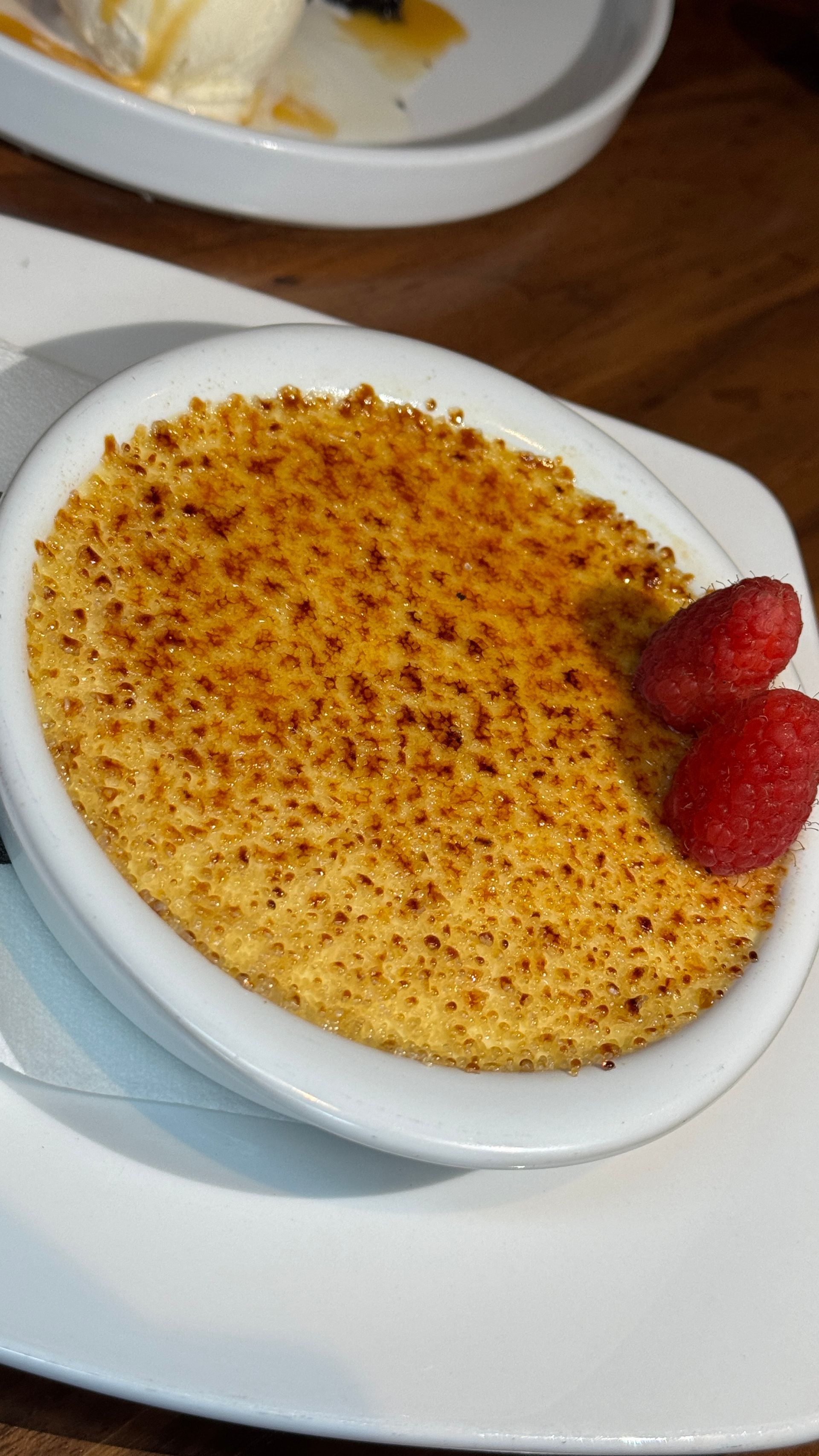 Crème brûlée in white dish, with caramelized sugar topping and raspberries.