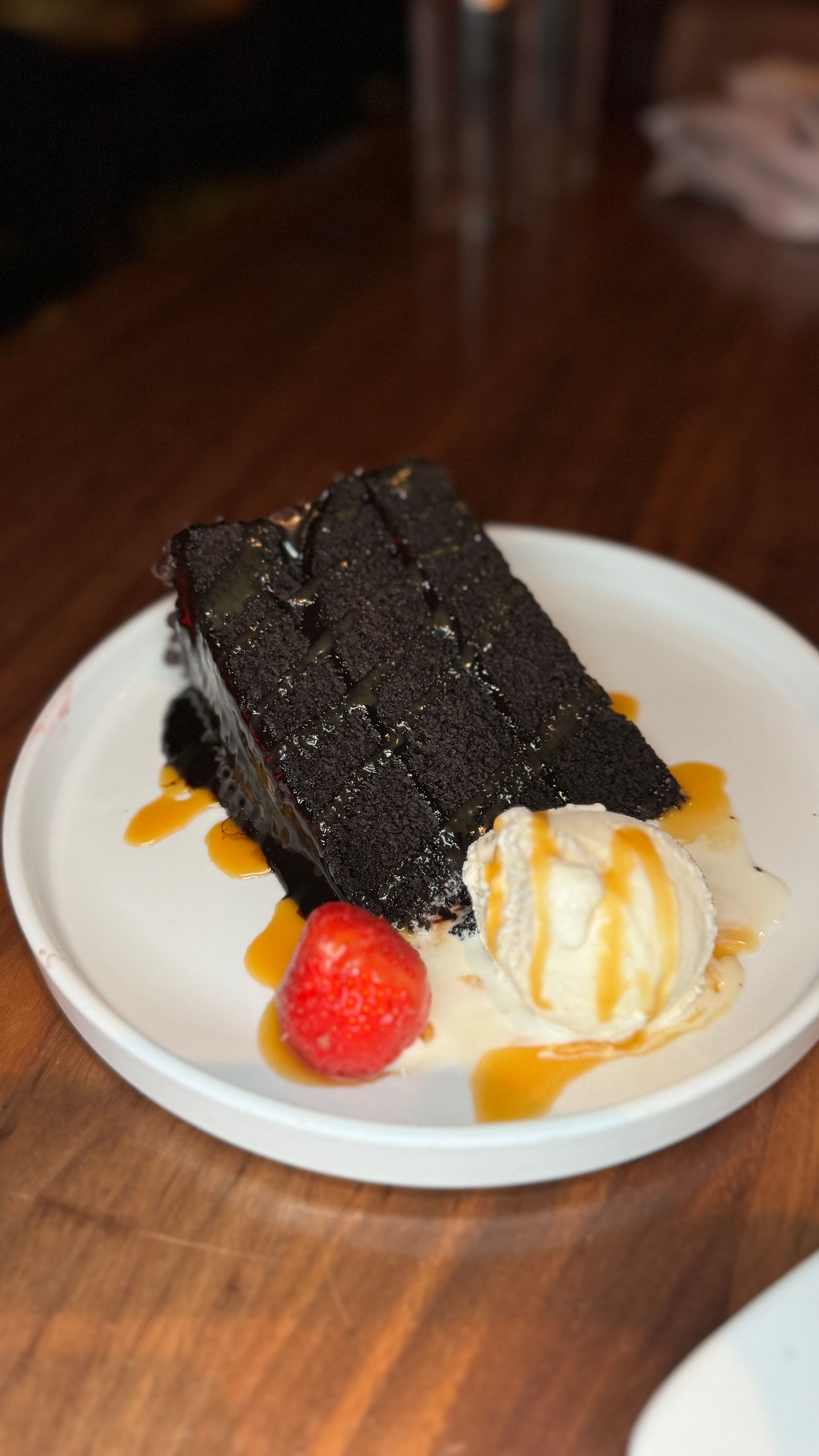 Chocolate cake slices with ice cream, caramel sauce, and a strawberry on a white plate.