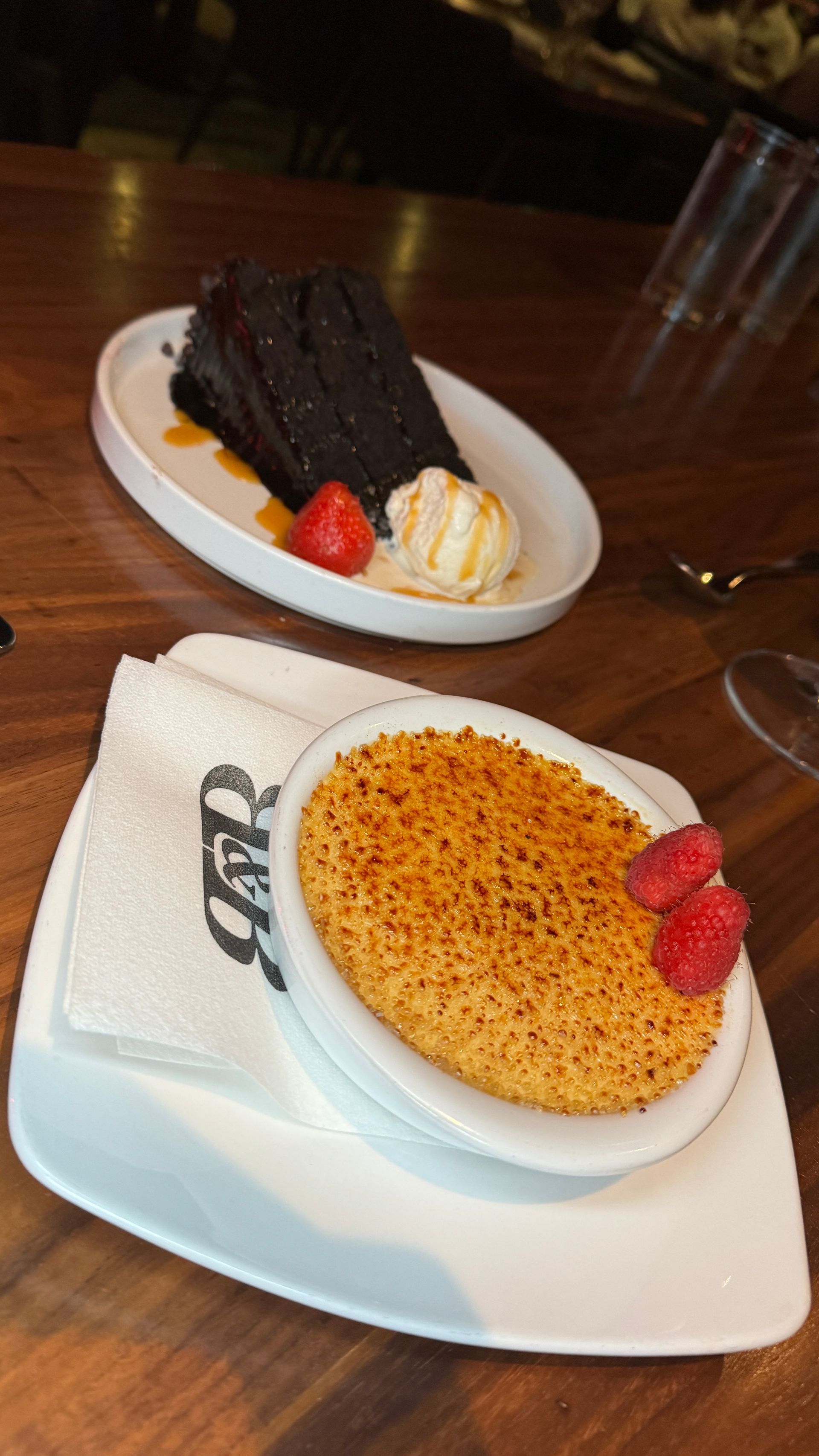 Two desserts on plates: Chocolate cake with ice cream, and creme brûlée with raspberries.