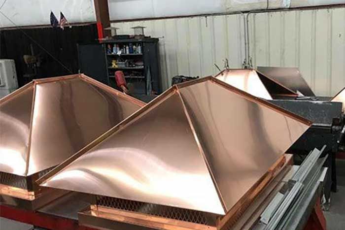 Copper chimney caps in a workshop, with a polished, reflective finish.