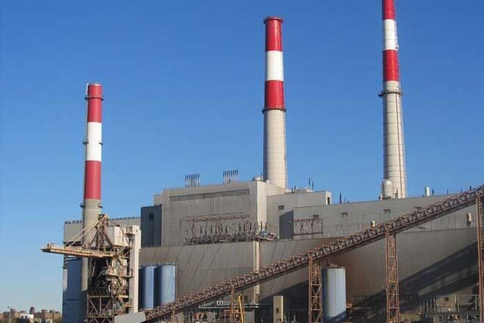 Power plant with three tall smokestacks, red and white striped, against a clear blue sky.