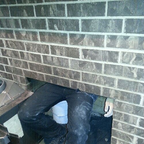 Person, wearing black pants, working through an opening in a brick wall. A bucket is visible.