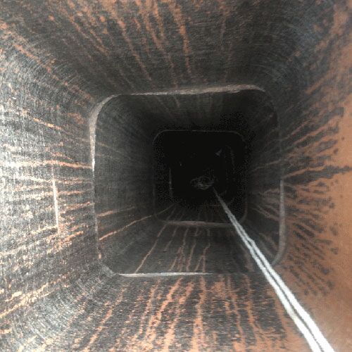 Looking up a dark, square chimney. Smoky soot covers the interior. A white rope hangs down.