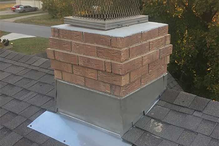 Brick chimney on a gray shingled roof with a metal cap and flashing.