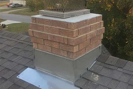 Brick chimney on a gray shingled roof with a metal cap and flashing.