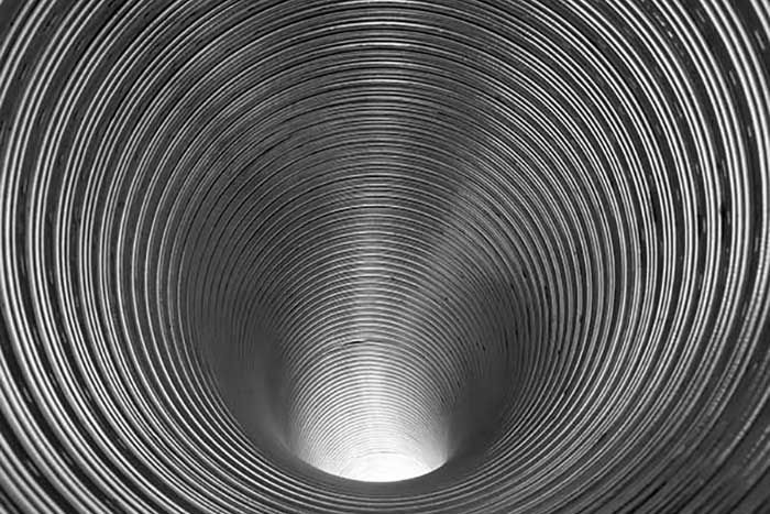 Inside view of a metallic, corrugated tube receding into a bright point.