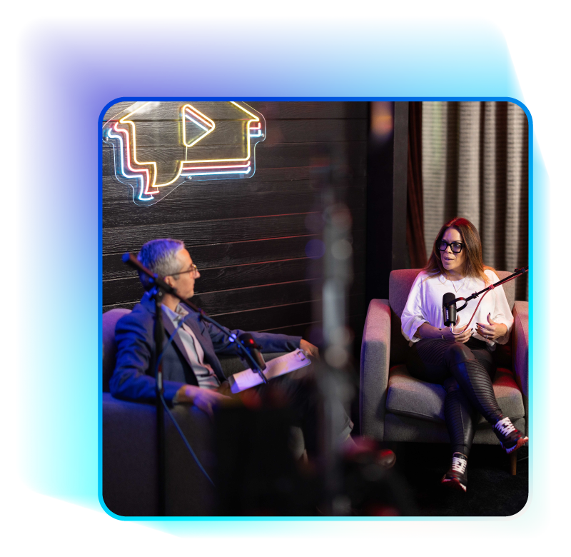 Podcast interview: man in suit and woman in white shirt seated with microphones in studio.