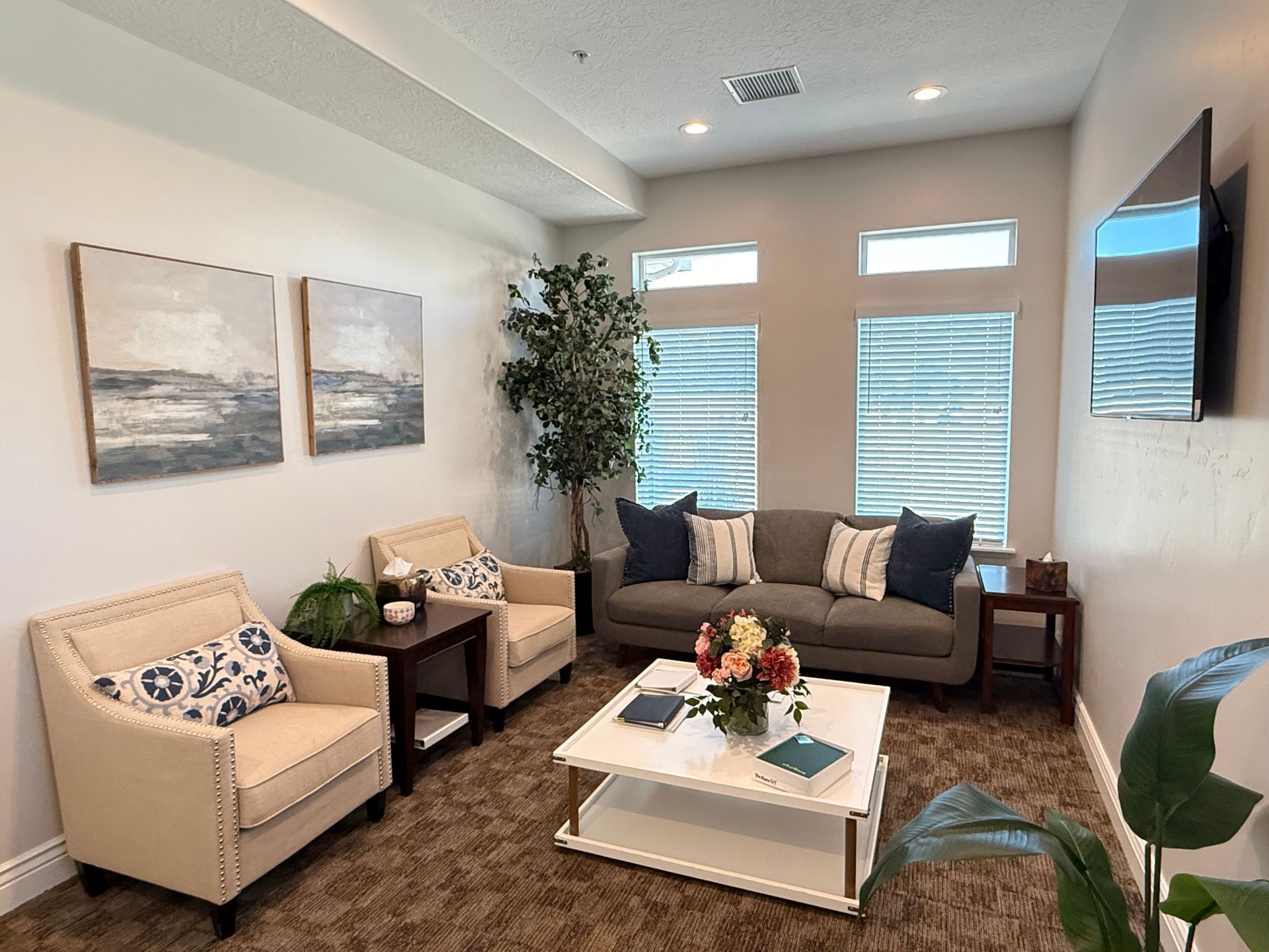 A waiting room with chairs, a sofa, coffee table, and art on the wall.