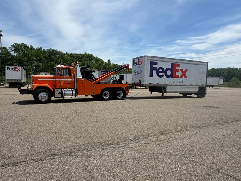 Tow truck towing a FedEx trailer across a parking lot under a cloudy sky
