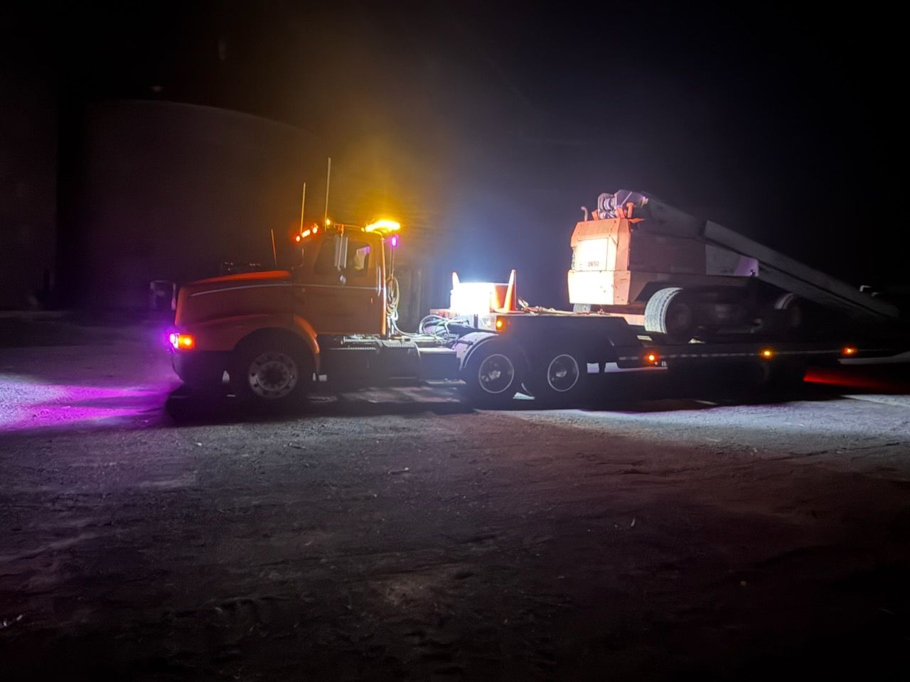 Tow truck with flashing lights at night, hauling a vehicle on a dark roadside