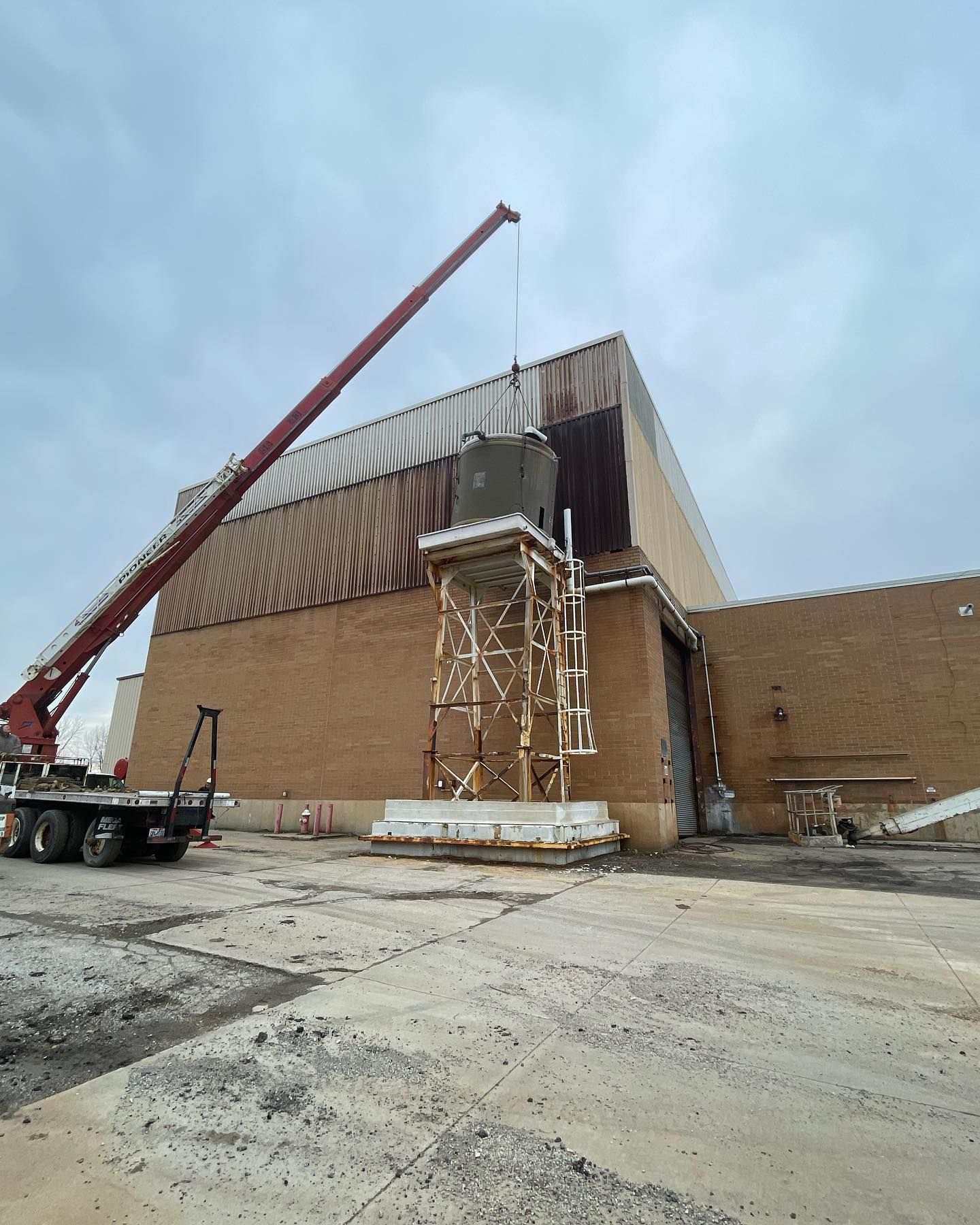 A crane lifting equipment near a large brick building on a cloudy day.