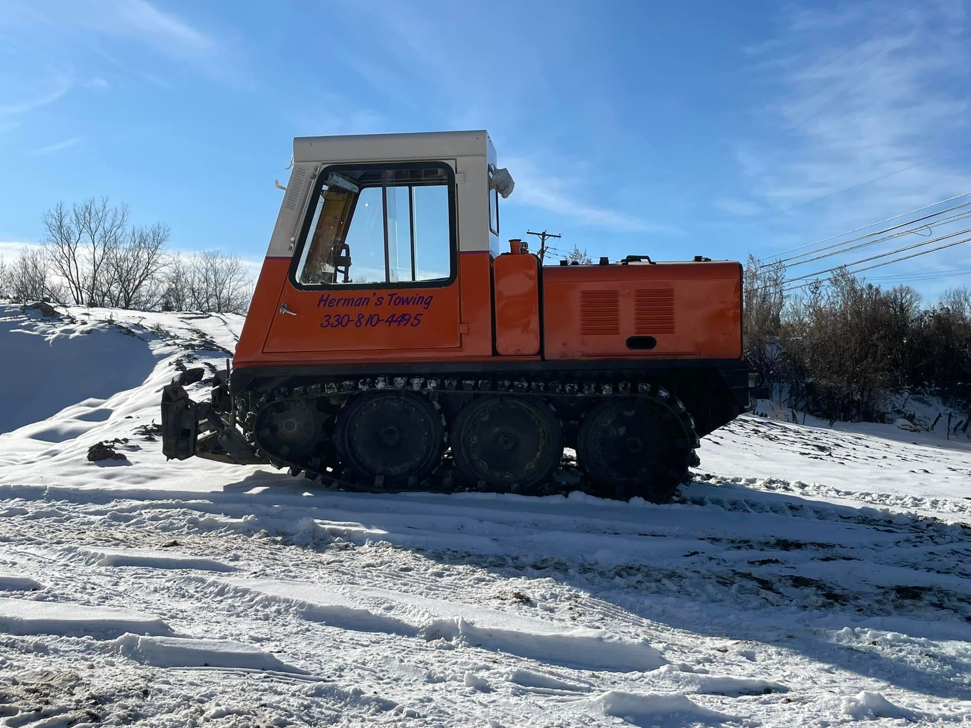 Orange snow groomer on snow, against a blue sky.