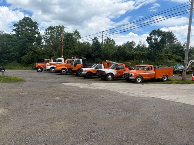 Several orange utility trucks parked in a gravel lot under a partly cloudy sky.
