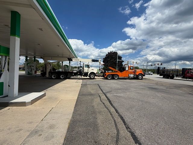 Orange tow truck at a gas station under a cloudy sky