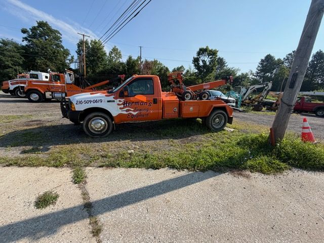 Orange tow truck parked on grass beside a road, with another tow truck in the background.