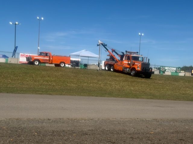 Orange tow trucks on a grassy hill near a road under a blue sky