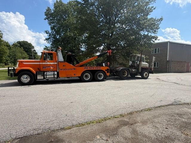 Orange tow truck hauling a black pickup in a parking lot beside a building and trees