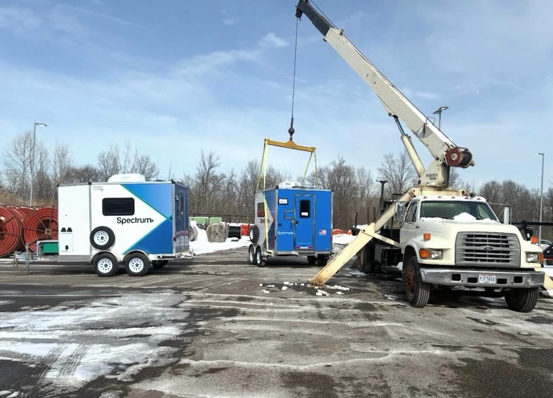 Crane lifting blue equipment truck in a snowy work yard with other utility vehicles nearby