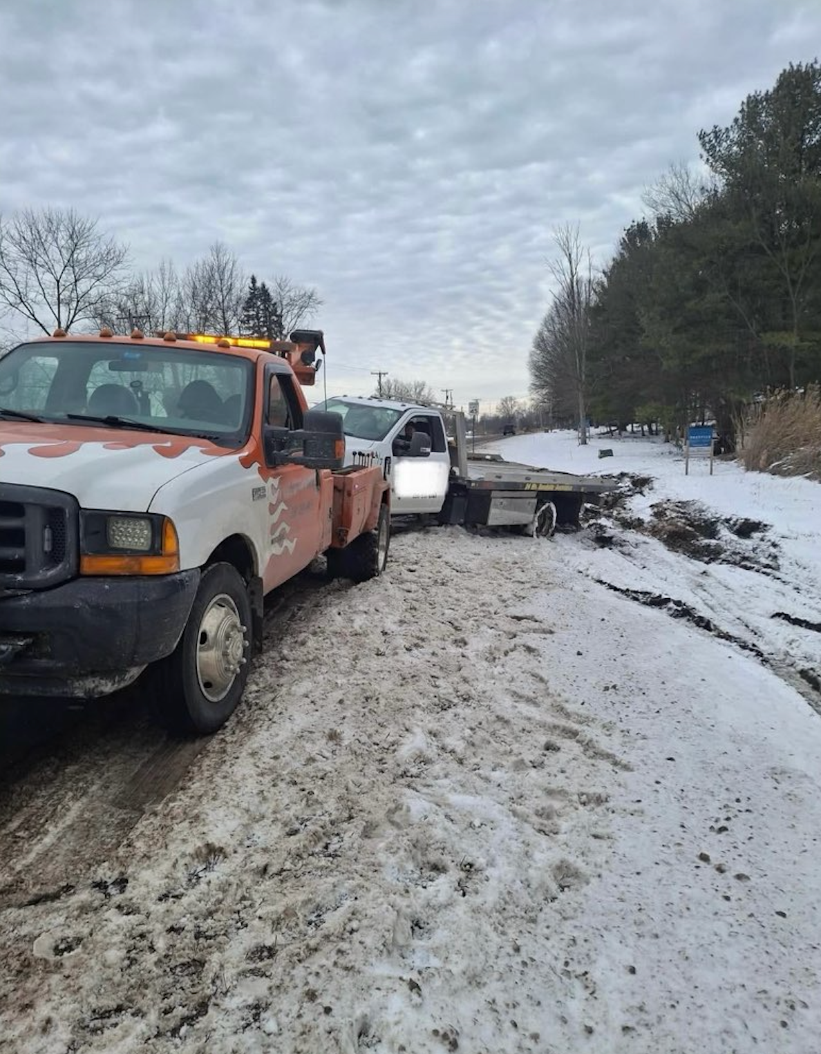 Tow truck hauling a car from a snowy roadside ditch on a winter road