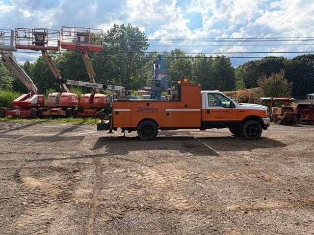 Tow truck loading a heavily damaged black car. A man secures straps. Sunny outdoor scene.