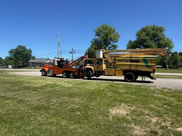 Orange tow truck and yellow utility truck parked on a roadside under a blue sky.