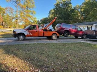An orange and white tow truck pulling a dark red SUV in a residential driveway on a sunny day.