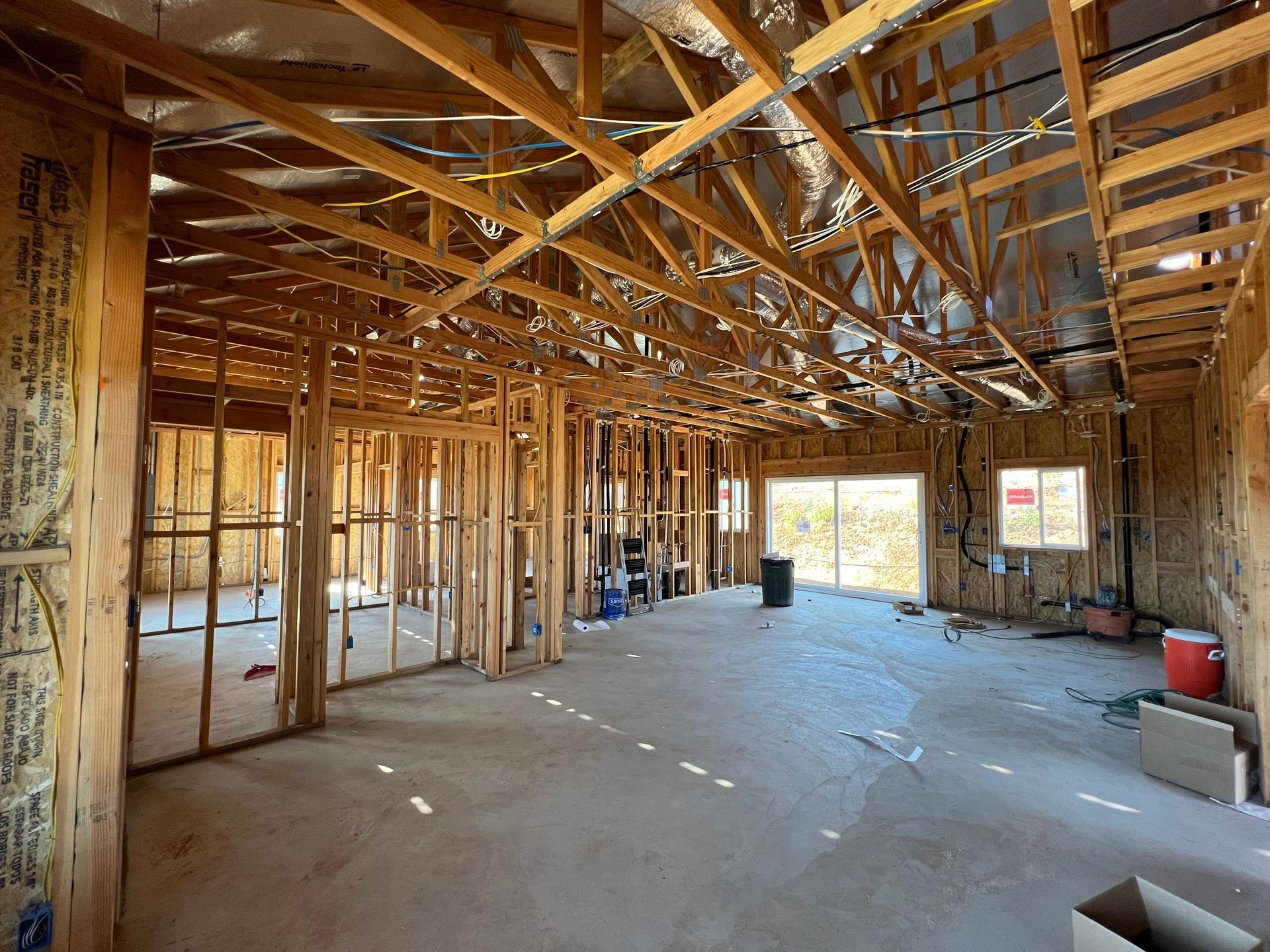 Interior view of a building under construction, with exposed wooden framing and a concrete floor.