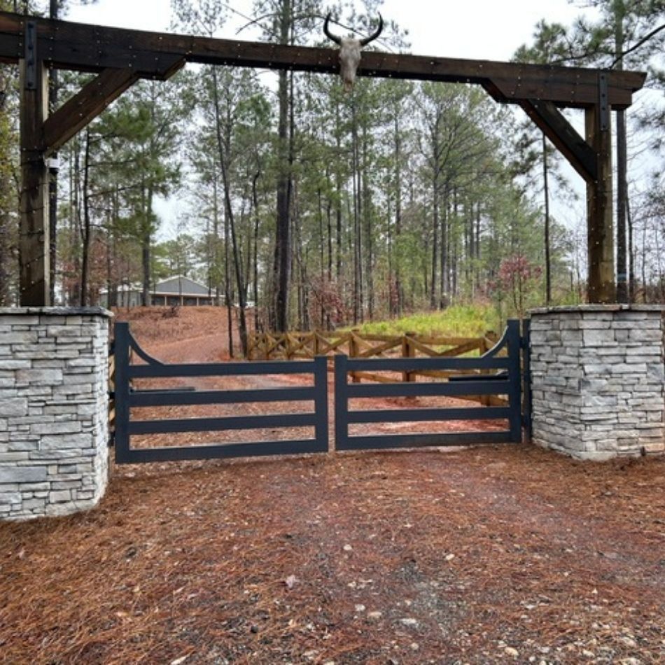 Black gate between stone pillars under a wooden archway at a forest entrance