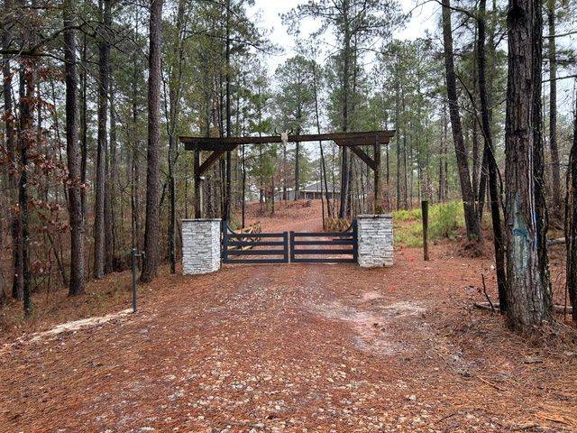Wooded driveway entrance with a wooden gate and stone pillars in a pine forest