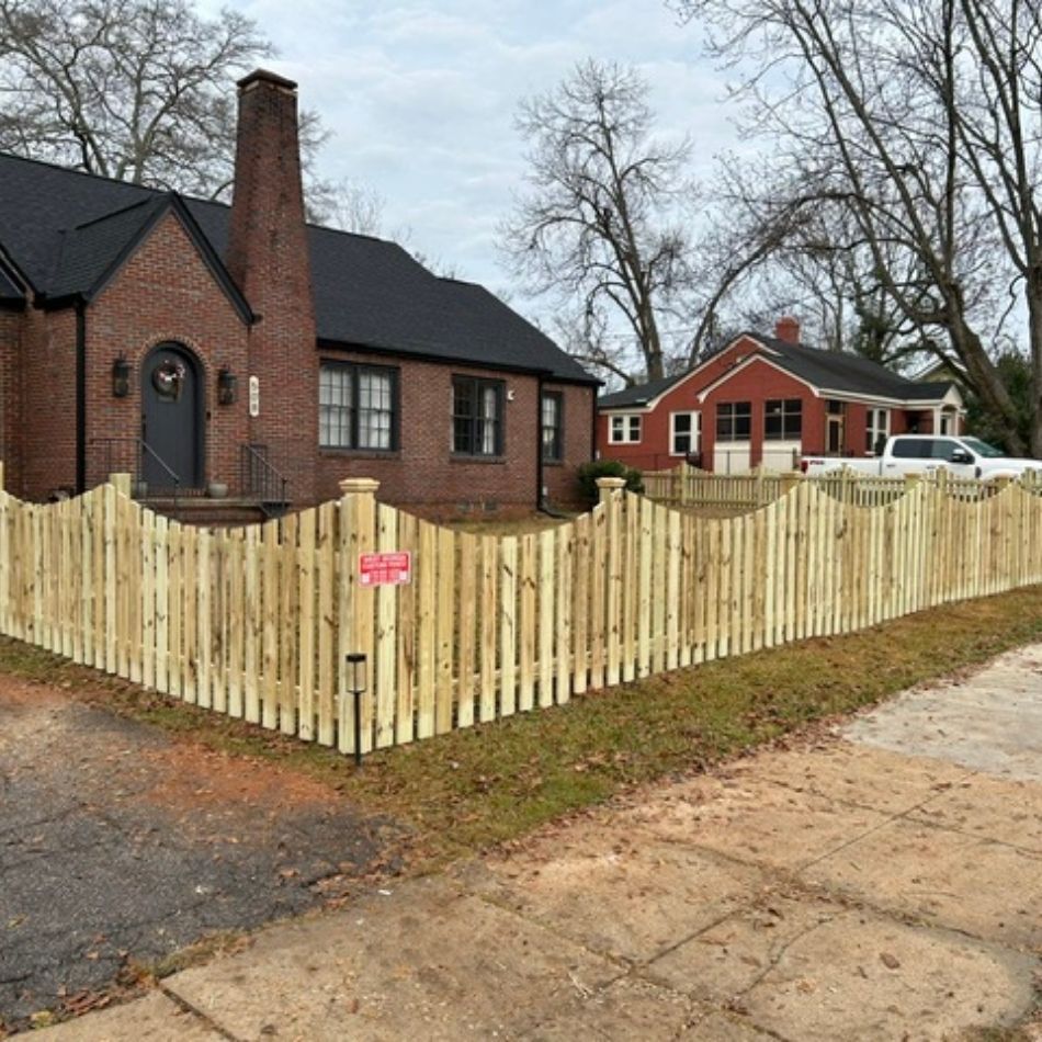 Brick house with a tall chimney and wooden privacy fence on a corner lot, with a red house in back.
