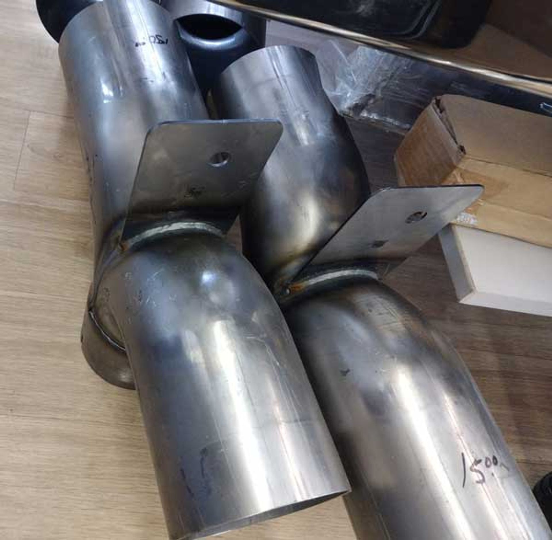 Two stainless steel pipes are sitting on a wooden floor